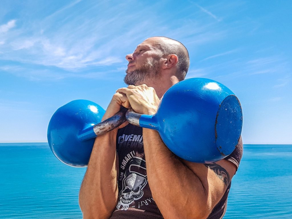 Bald man carrying blue kettle weights